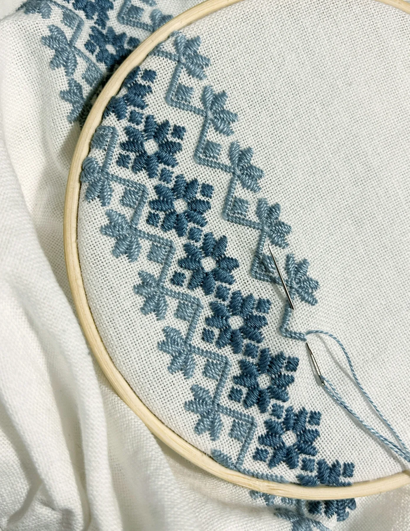 Blue embroidery on white fabric inside a hoop